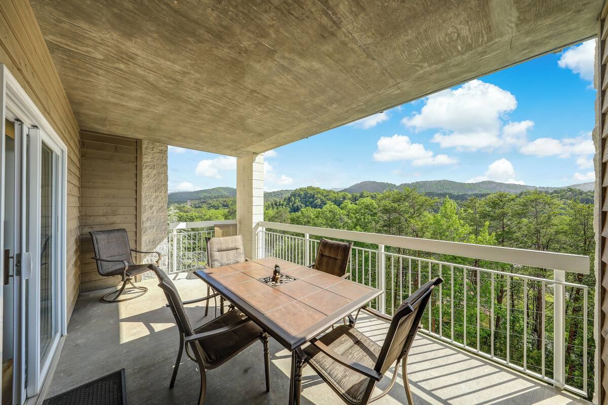 A balcony with a table and chairs, overlooking a forested landscape.