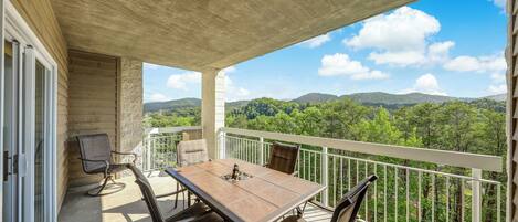 A balcony with a table and chairs, overlooking a forested landscape.