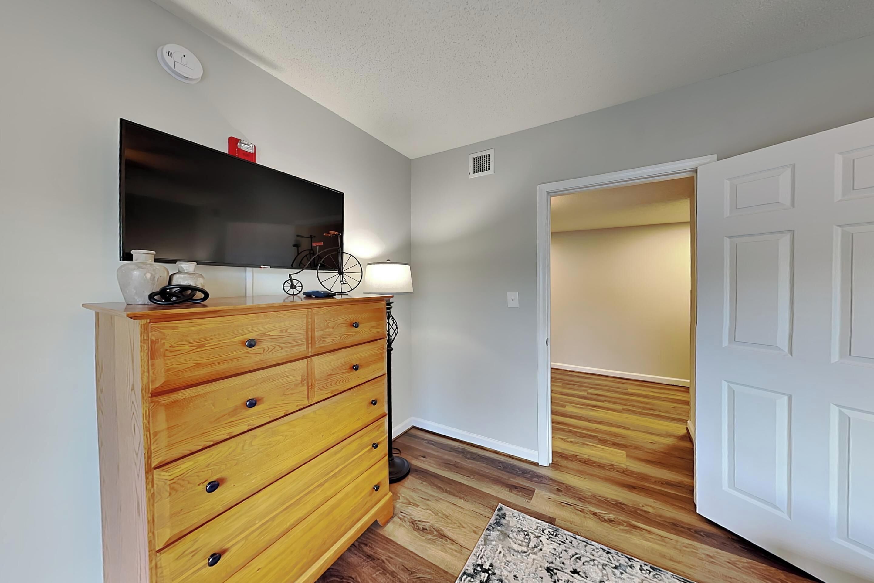 A hallway with a wooden dresser, a flat-screen TV, a lamp, and a patterned rug.