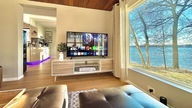A living room with a television, a window with a view of trees and water, and a sofa.