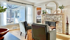 A living room with a fireplace, two armchairs, a coffee table, and a large window.