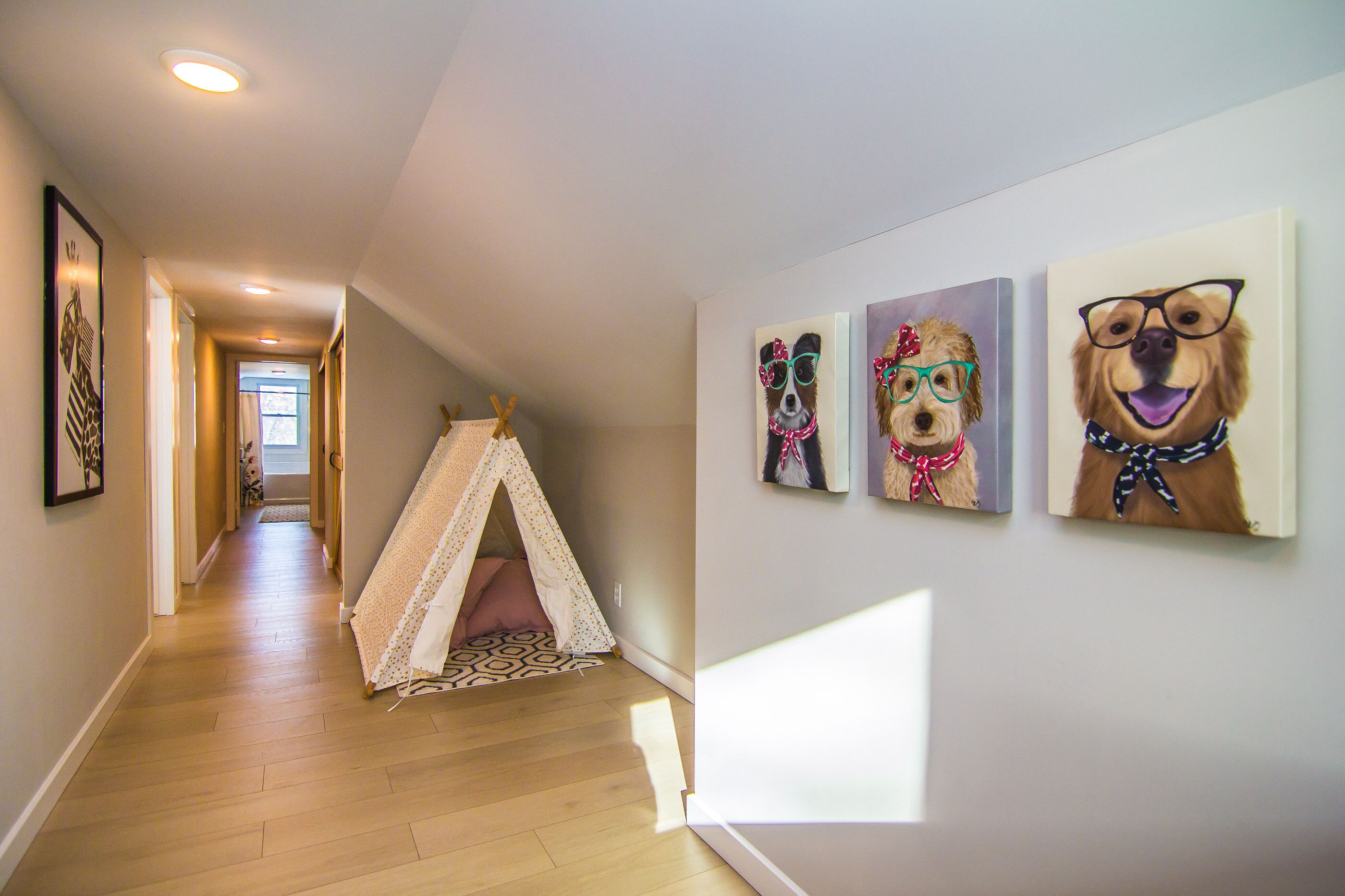 A hallway with a wooden floor, a tent-like play area, and three framed paintings of dogs on the wall.