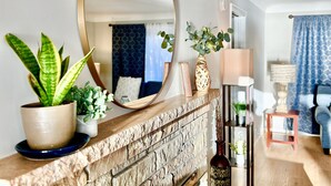 A living room with a stone fireplace, a large mirror, and various plants.