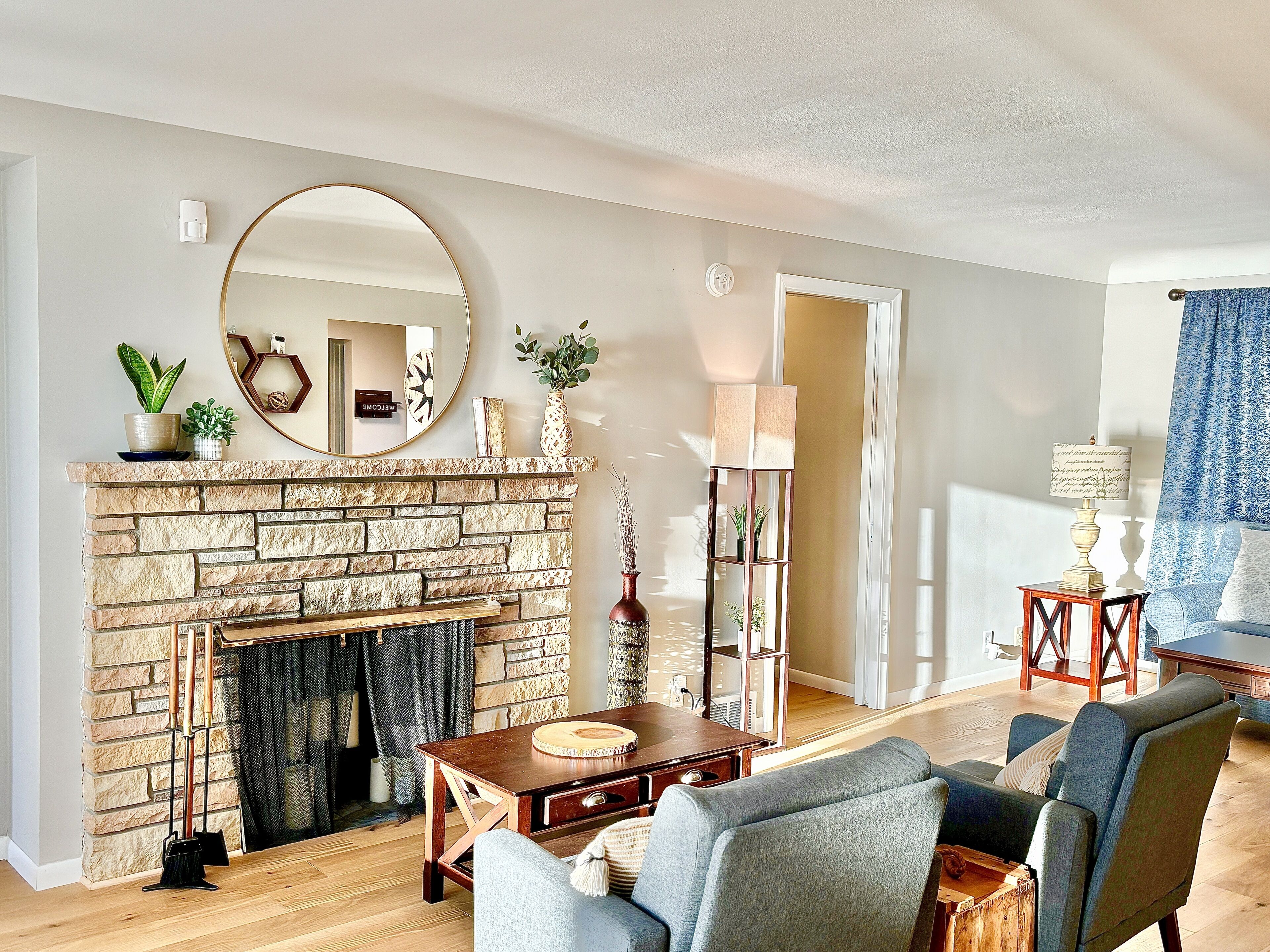 A living room with a stone fireplace, a round mirror, a coffee table, and a blue sofa.