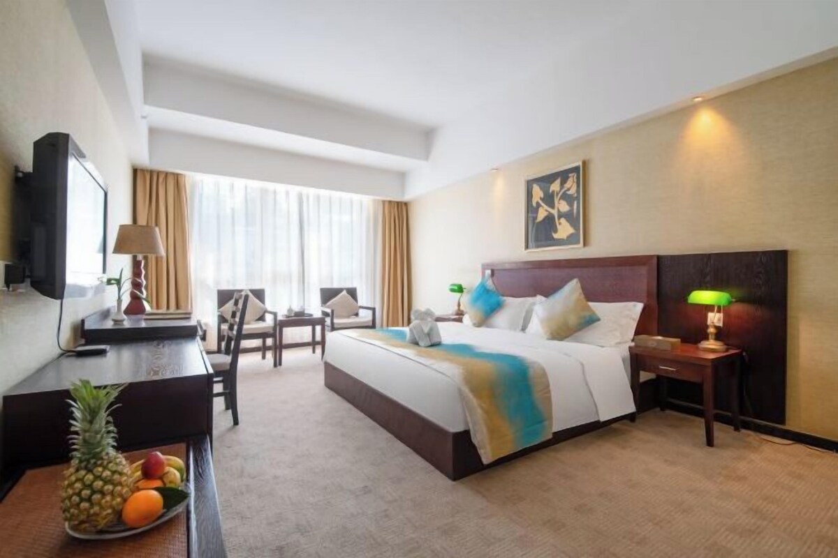 A hotel room with a bed, bedside table, lamp, desk with a computer, chair, and a fruit bowl.