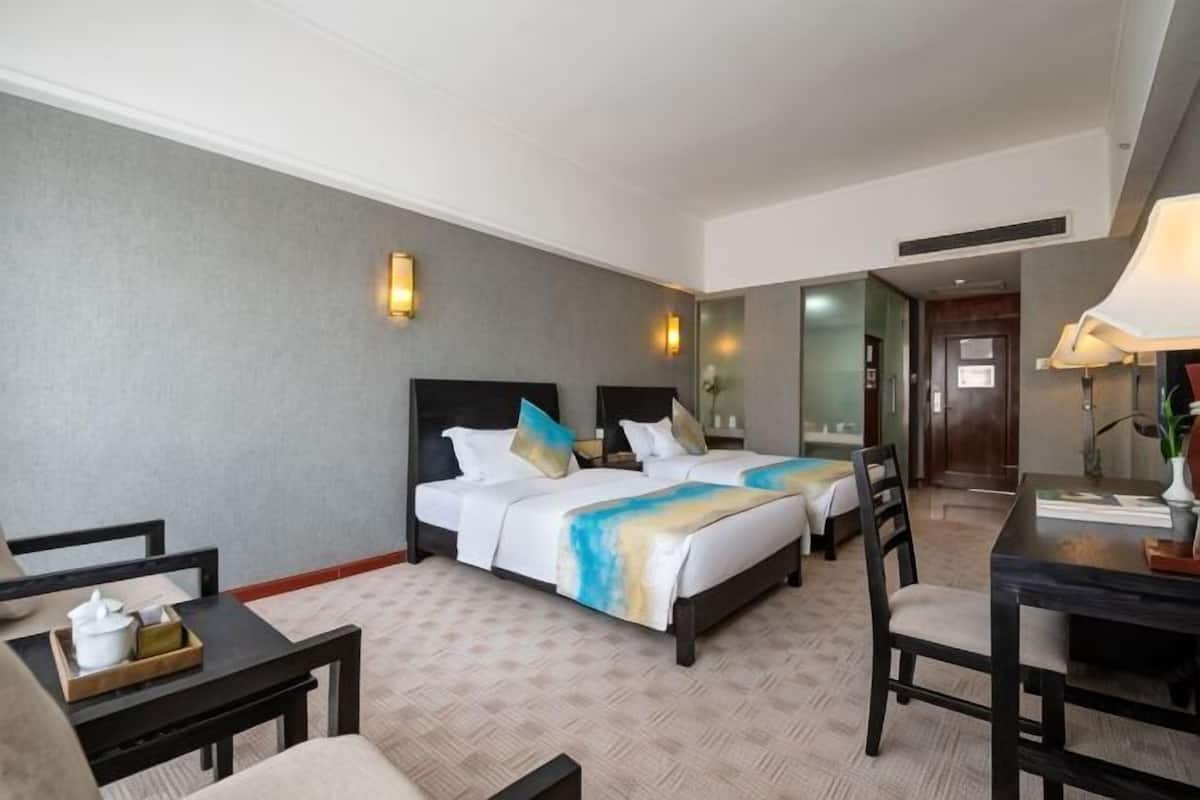 A hotel room with two beds, a desk, a chair, and a small table.