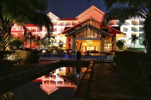 A hotel with a central building, a reflecting pool, and palm trees.