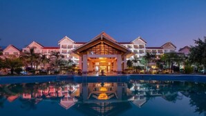 Un complexe hôtelier doté d’un bâtiment central qui se reflète dans une piscine, entouré de plusieurs villas.
