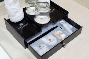 Une boîte de rangement noire, dotée de compartiments contenant divers objets, notamment une serviette blanche et des récipients en verre avec des couvercles.
