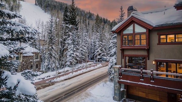 A two-story lodge with a stone facade and large windows, surrounded by snow-covered trees and a mountain backdrop. - Ski-in/Out Elegance in Beaver Creek | Chalet Bello (Beaver Creek)