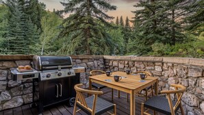 Patio esterno con barbecue Weber, tavolo di legno e quattro sedie.