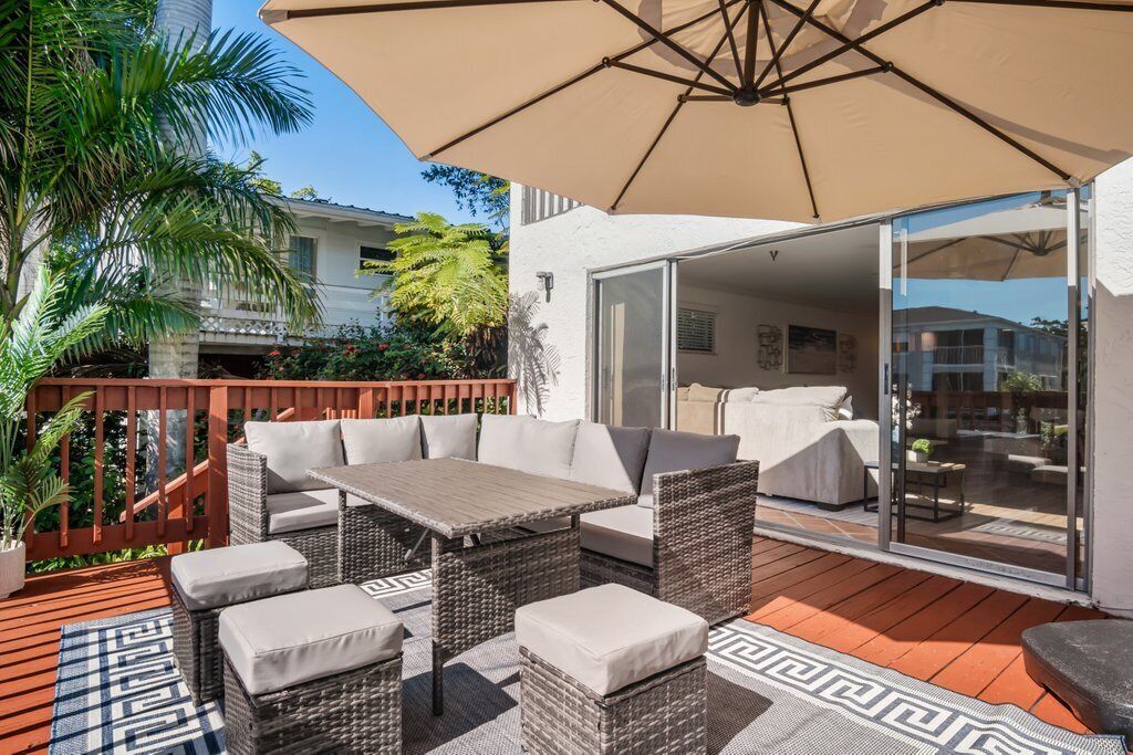 Une terrasse extérieure aménagée avec des meubles en osier, un grand parasol et une vue sur l’immeuble voisin.