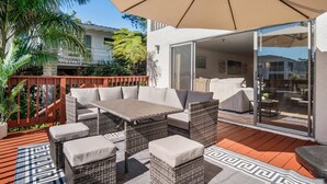 Patio esterno con mobili in vimini, un ombrellone grande e vista sull'edificio adiacente.