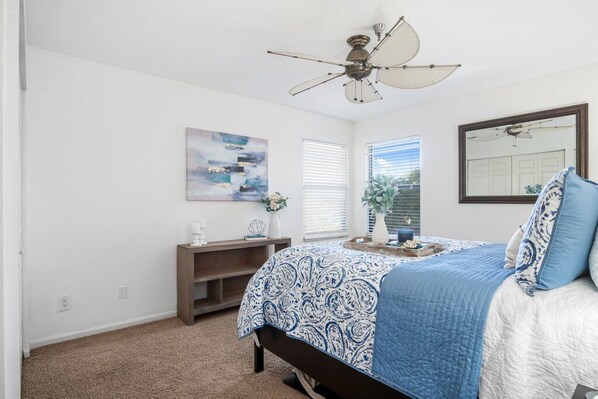 A bedroom with a bed, a ceiling fan, a window with blinds, a small shelf, and a painting on the wall. - Exceptional Waterfront Condo in Downtown Naples! (Naples)