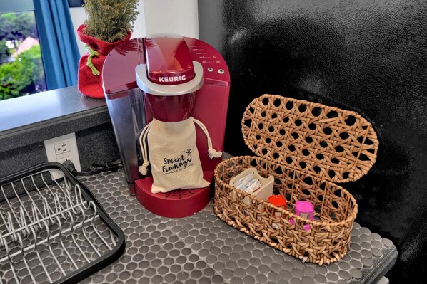 Une machine à café Keurig rouge, un panier en osier contenant des articles de toilette et une petite plante en pot sur un comptoir de cuisine.