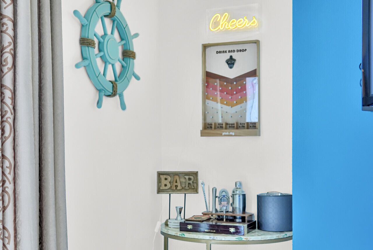 A wall with a nautical-themed decor including a ship's wheel, a neon 'Cheers' sign, a 'Drink and Drop' poster, and a 'BAR' sign.