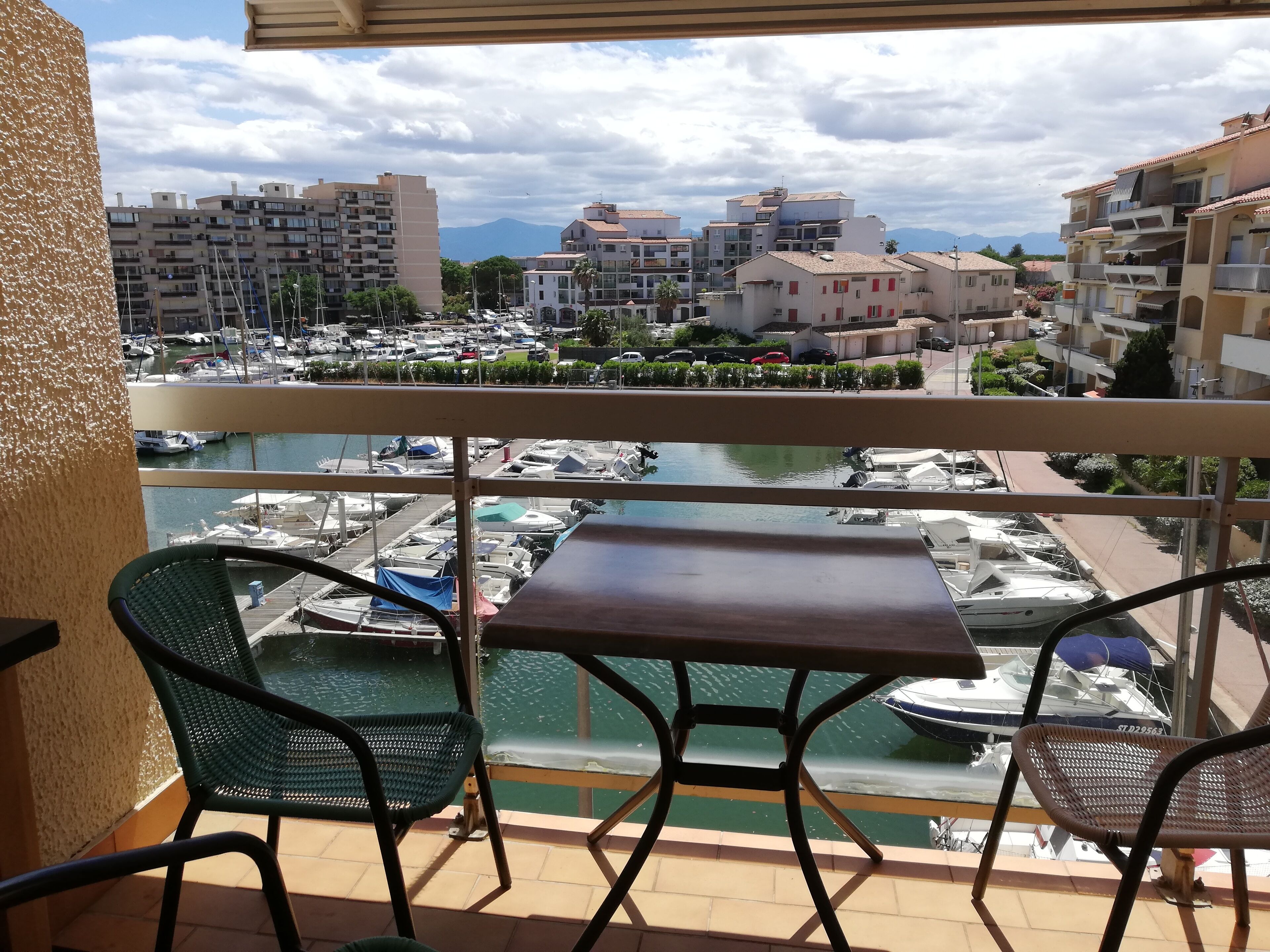 A balcony with a table and chairs overlooking a marina with boats and buildings in the background.