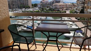 Ein Balkon mit Tisch und Stühlen mit Blick auf einen Yachthafen, umgeben von Wohnhäusern und einem Berg im Hintergrund.