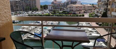 A balcony with a table and chairs overlooking a marina with boats and buildings in the background.