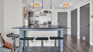 Una cocina moderna con una isla central, taburetes de bar, iluminación colgante y un horno empotrado.