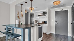 Una cocina moderna con una isla central, taburetes de bar, iluminación colgante y horno empotrado.