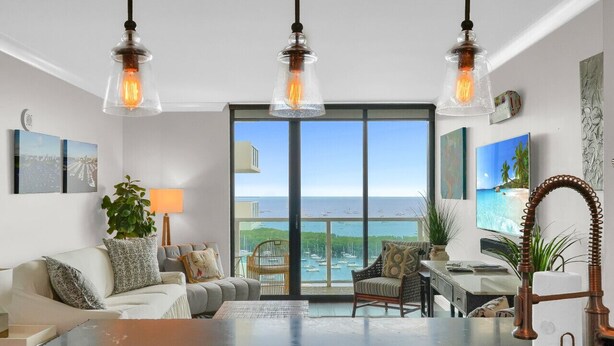 Un salón amplio con un ventanal grande con vistas al mar, un sofá cómodo, una mesa de centro y un escritorio con una lámpara.