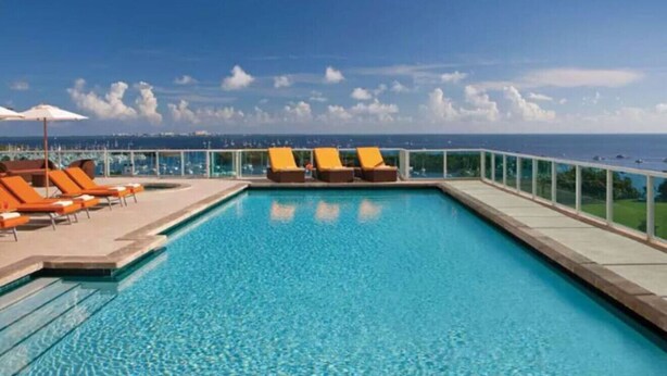 A rectangular pool with clear blue water, surrounded by orange lounge chairs and a glass railing. - SF Amazing Studio - Walking Distance to Cocowalk (Miami)