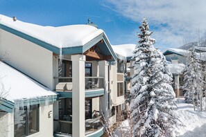 Un hotel a più piani con balconi, tetti imbiancati dalla neve e un grande abete sempreverde in primo piano.