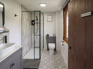 A bathroom with a glass shower enclosure, a toilet, a sink, and a wooden door labeled "BATHROOM".