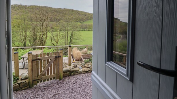 A view from a balcony with a stone wall and wooden gate, overlooking a green landscape with trees and hills. - Pengeulan (Machynlleth)