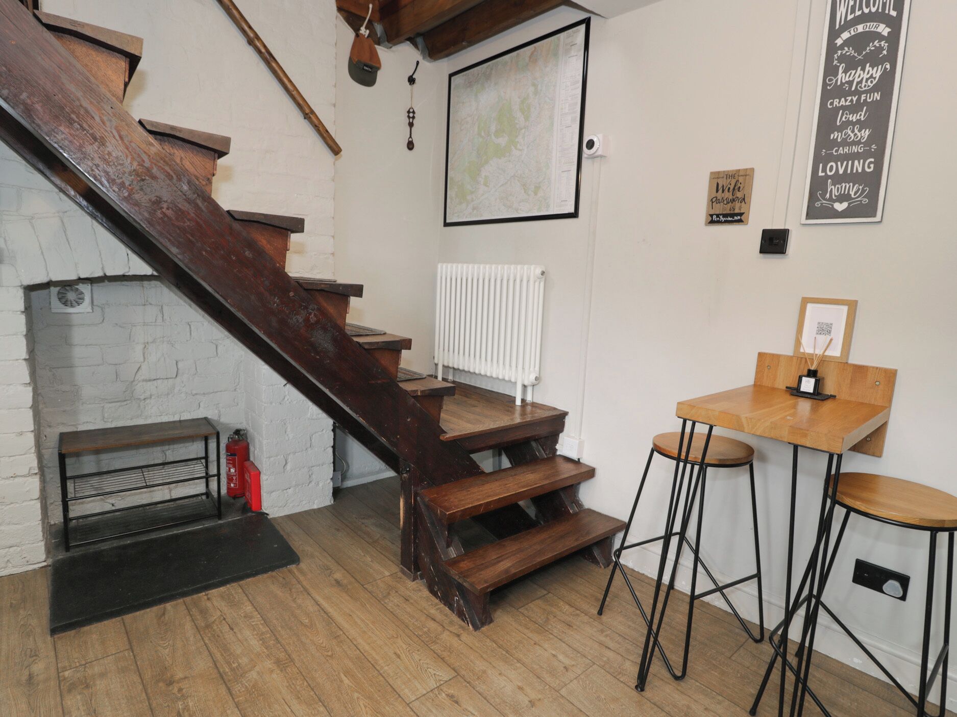 Un escalier menant à une mezzanine, avec un radiateur blanc et une carte accrochée au mur.