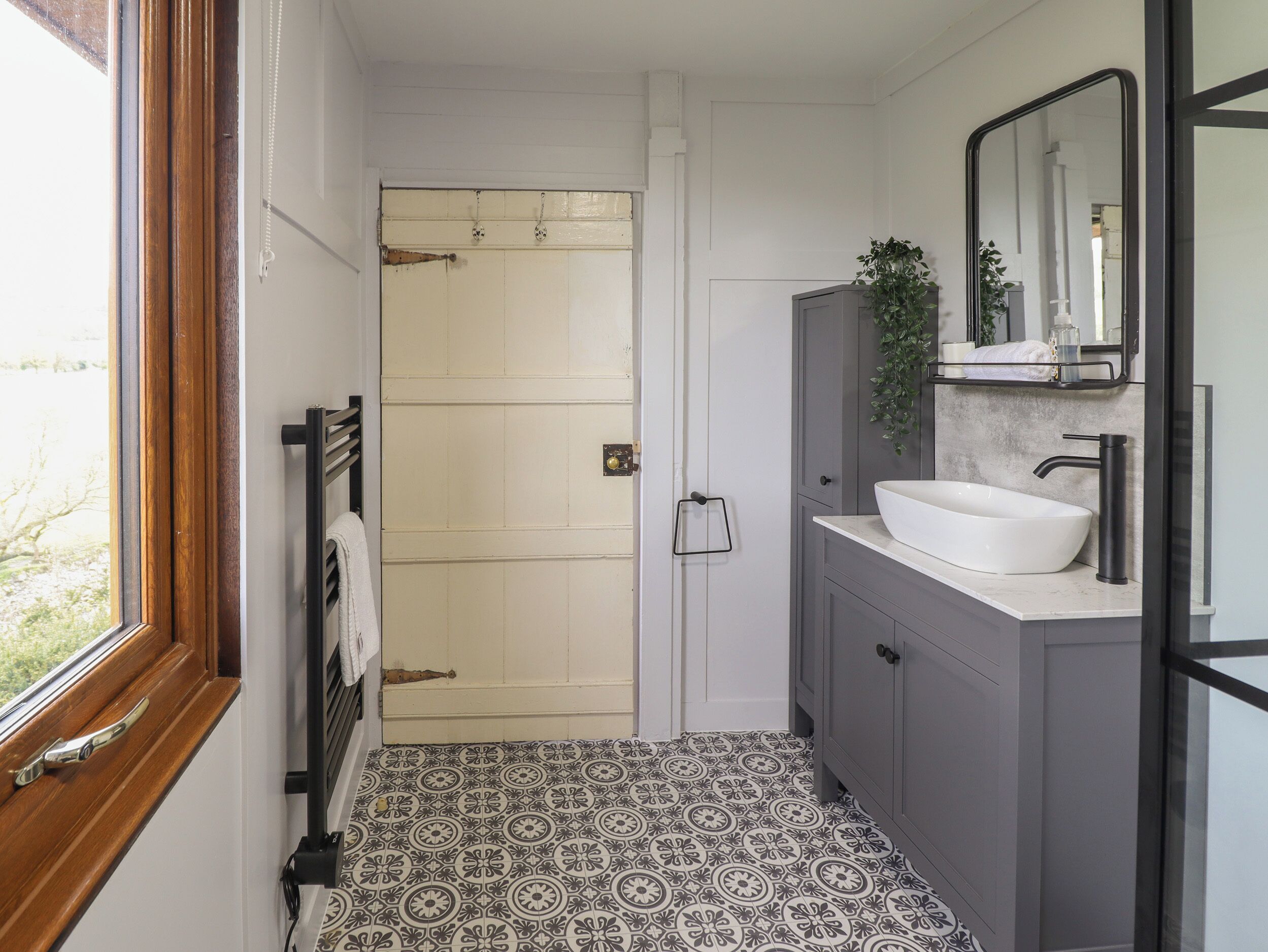 Une salle de bain avec une porte blanche, une fenêtre, un lavabo et un miroir.