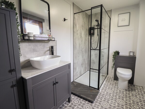A modern bathroom with a large white vessel sink, dark cabinets, a glass shower enclosure, and patterned floor tiles. - Pengeulan (Machynlleth)