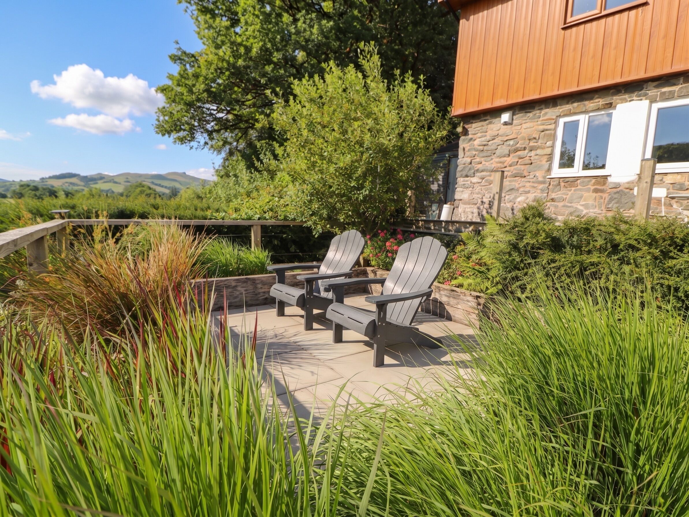 A patio with Adirondack chairs, a stone wall, and a view of hills.