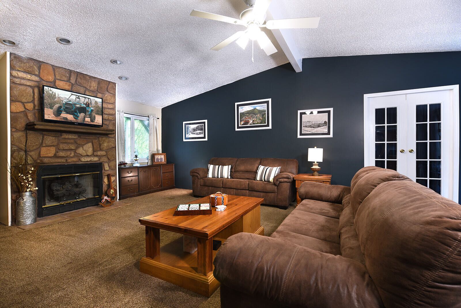 A living room with a stone fireplace, a brown sofa set, a wooden coffee table, and framed pictures on the wall.