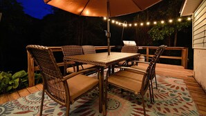 Eine Terrasse im Freien mit Tisch, Stühlen, Lichterkette und einem großen Sonnenschirm.