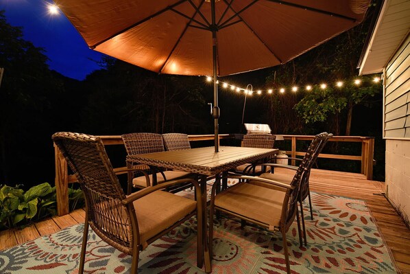An outdoor patio with a table and chairs, string lights, and a large umbrella.