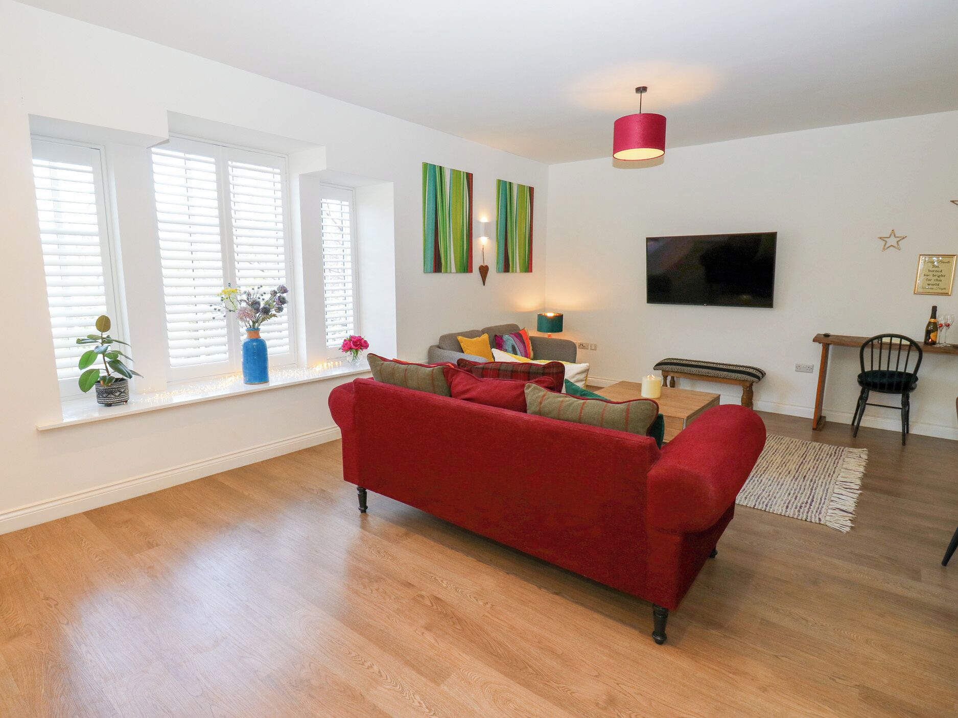 A modern living room with a red sofa, a flat-screen TV, and a dining area with a wooden table and chairs.