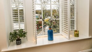 A window with white shutters, a potted plant, a blue vase, and a candle on the ledge. - Over The Arch (Keighley)