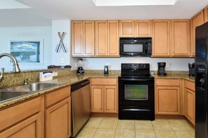 A kitchen with wooden cabinets, a microwave, a stove, a dishwasher, and granite countertops. - 11th Floor FULL 2 Bedroom at The Palms of Destin (Destin)