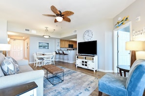 A living room with a ceiling fan, a TV, a dining area, and a kitchen. - 11th Floor FULL 2 Bedroom at The Palms of Destin (Destin)