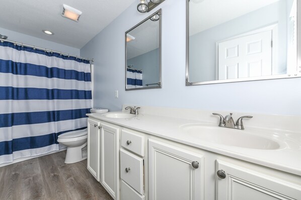 A bathroom with a white vanity, two sinks, a mirror, and a striped shower curtain.