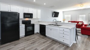 A modern kitchen with white cabinets, black appliances, and a wooden floor.