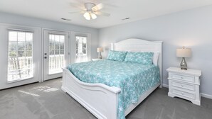 A bedroom with a white bed, a nightstand, a ceiling fan, and a view through the door.