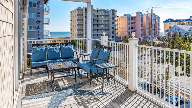 Ein Balkon mit einer Couch, Stühlen und einem Tisch, mit Blick auf einen Strand und Gebäude.