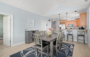 Een moderne keuken met houten kasten, een eethoek met een donker vloerkleed en een keukeneiland.