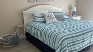 A bedroom with a bed, a nightstand, a lamp, and wall decorations. - Beach Front Condo (Bonita Springs)