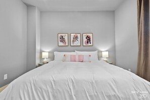 Une chambre à coucher moderne avec un grand lit, deux tables de chevet avec des lampes et trois œuvres d’art encadrées accrochées au mur.