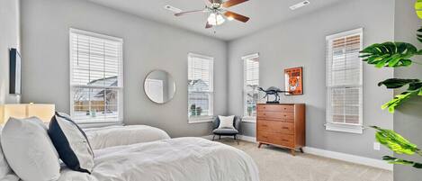 A bedroom with two beds, a dresser, a chair, and a ceiling fan.