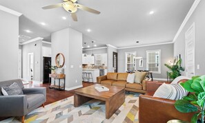 A spacious living room with a gray sofa, a wooden coffee table, and a brown leather sofa. There is a kitchen area in the background with white cabinets and a dining table. - The Broadway SLEEPS 10 Near Pleasant Grove (Rogers)